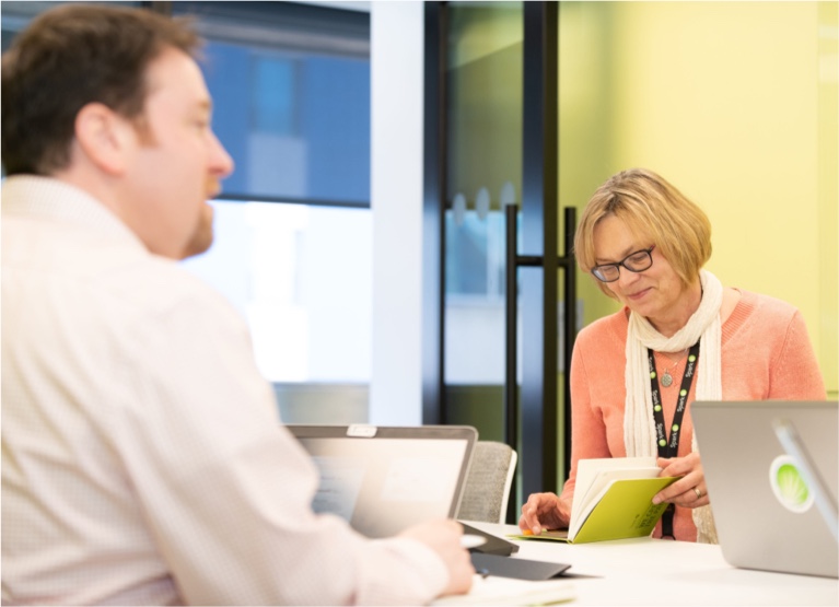 Spark Therapeutics Medical Affairs team member sitting at a conference table, working on a laptop and smiling at the team member next to him who is working on a laptop and smiling